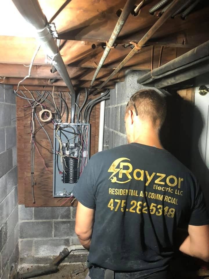A Rayzor Electric electrician working on an electrical panel in a basement
